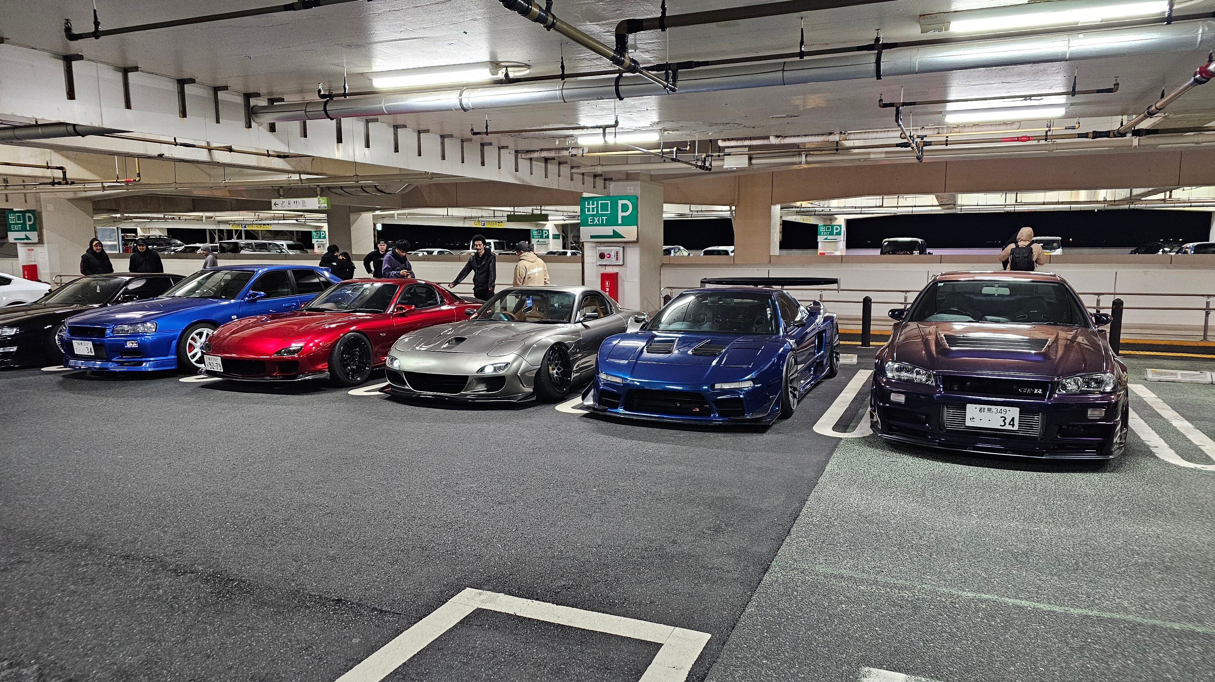 Two R34 GTRs, a widebody RX7, and a widebody Honda NSX parked at Umihotaru Parking Area in Japan