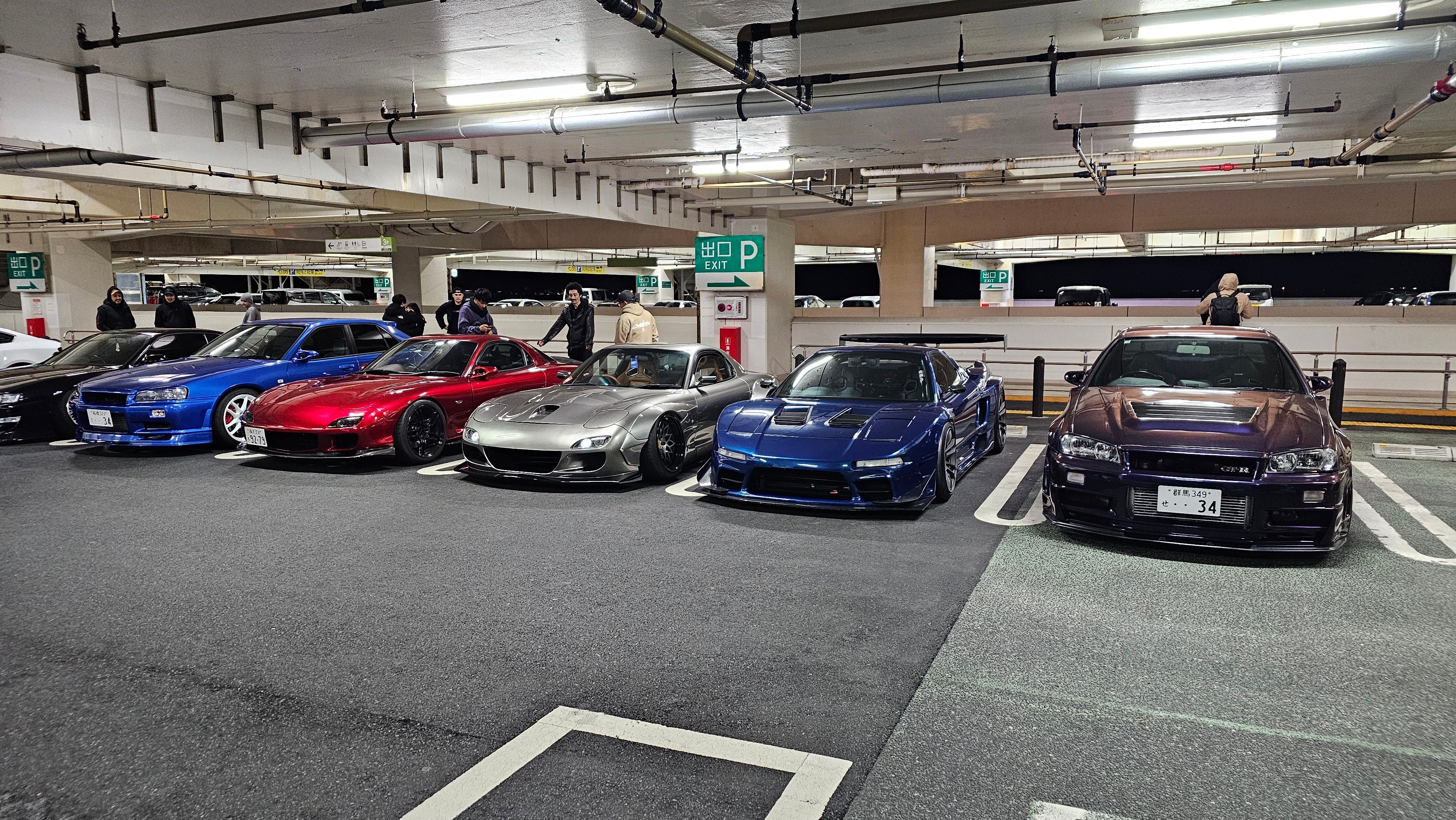 Two R34 GTRs, a widebody RX7, and a widebody Honda NSX parked at Umihotaru Parking Area in Japan